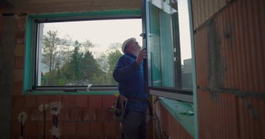 Elle çalışan kişi, konut inşaatı alanındaki pencere montajını, çerçeve hizalamasını ve güvenli kurulum için kalite standartlarını denetliyor