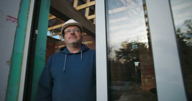 İnşaat projesinde inşaat alanında tecrübeli bir inşaat işçisi çerçevenin altından kendine güveniyor, odak noktasını ve profesyonelliğini gösteriyor.