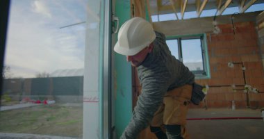 Yerleşim yerinin kalite kontrolü, sert şapkalı işçi hassasiyet ve güvenlik için pencere kurulumunu denetliyor