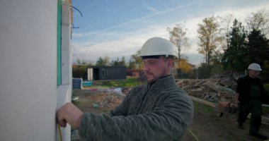 İnşaat halindeki bir binanın pencere çerçevesini bant ile ölçen işçiler, hassas ölçümler, odaklı işçilik, inşaat ilerlemesi, dış proje kurulumu