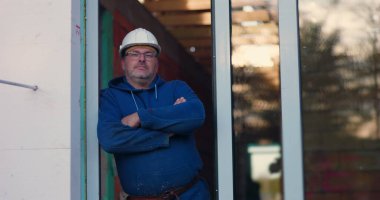 Kolları çapraz duran inşaat işçisi, başlık ve gözlük takıyor, kendine güvenen ifade, inşaat projesi, inşaat alanını denetliyor.