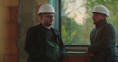 Kapalı alan inşaatı, takım çalışması ve işbirliği, gevşek atmosfer gibi pencerelerin önünde gelişigüzel sohbet eden iki inşaat işçisi.