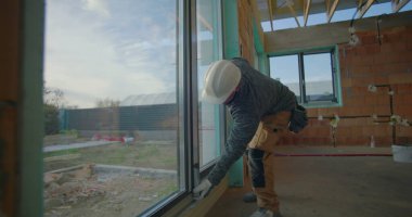 Yerleşim yerinin kalite kontrolü, sert şapkalı işçi hassasiyet ve güvenlik için pencere kurulumunu denetliyor