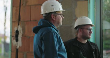 İnşaat işçileri inşaat başlıklarını düzeltiyor, iş, grup tartışması, kapalı inşaat alanı, güvenlik donanımı, bina yenileme alanında takım çalışması hazırlıyorlar.