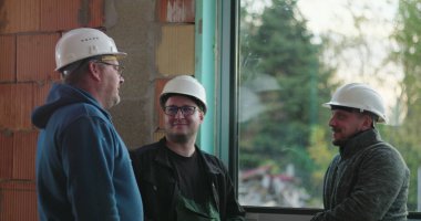 İnşaat işçileri inşaat başlıklarını düzeltiyor, iş, grup tartışması, kapalı inşaat alanı, güvenlik donanımı, bina yenileme alanında takım çalışması hazırlıyorlar.