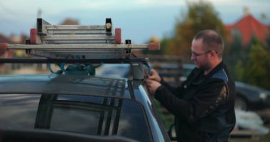 Çalışanlar merdiveni arabanın çatı rafına yerleştiriyor, ulaşıma, açık havaya, inşaat aletlerine, güvenlik ekipmanlarına, yerleşim alanının geçmişine hazırlanıyor.