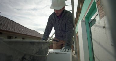 Kovadan havan topu çıkarmak, dış duvardaki yalıtım işleri için güvenlik donanımlı inşaat işçisi, arka planda kask, eldiven ve merdiven ile yakın plan.