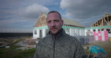 İnşaat alanındaki işçinin portresi, kameraya güvenle bakmak, arka planda inşaat halindeki konut yapısı