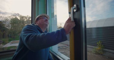 İşçi inşaat alanında pencere çerçevesinin hizalanmasını sağlamak için seviye aracı kullanıyor, sabit kasklı odaklı işçinin yakın plan pencere açılışı yakınlarındaki ölçümleri ayarlıyor