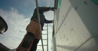 Dış duvara yalıtım paneli yerleştiriliyor. İnşaat işçisi iskelede çalışıyor. Tam konum için elleri kullanıyor.