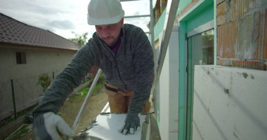 İskele üzerinde havan topu, miğferli inşaat işçisi ve arka planda merdiven, konut binasının ön cephesinde yalıtım için hazırlık