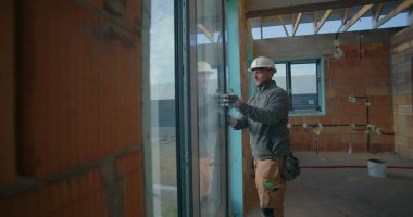 Konut inşaatı sırasında pencere kurulumunu denetleyen işçiler, başlık takarak, yerleşim yerinde hizalama ve kalite standartları sağlayarak,