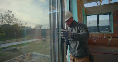 Konut inşaatı sırasında pencere kurulumunu denetleyen işçiler, başlık takarak, yerleşim yerinde hizalama ve kalite standartları sağlayarak,