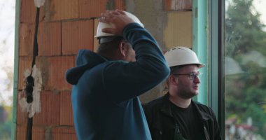 İnşaat işçileri inşaat başlıklarını düzeltiyor, iş, grup tartışması, kapalı inşaat alanı, güvenlik donanımı, bina yenileme alanında takım çalışması hazırlıyorlar.