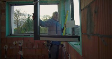 Elle çalışan kişi, konut inşaatı alanındaki pencere montajını, çerçeve hizalamasını ve güvenli kurulum için kalite standartlarını denetliyor