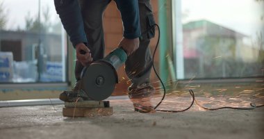 Açı öğütücüyle beton öğüten, kıvılcımlar yaratan, koruyucu kask takan, malzeme kesimine yoğun odaklanan, iç inşaat projesi