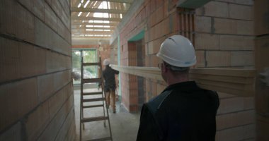 İnşaat işçileri miğferleriyle inşaat halindeki ahşap kalasları, taşınan malzemeleri, inşaat projesindeki takım çalışmasını ve organizasyonu taşıyorlar.