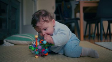 Bebek yerde yatıyor, ilginç bir şekilde renkli bir oyuncağı keşfediyor, güzel motor becerilerini geliştirirken çiğniyor, ev ortamında duyusal oyunlar oynuyor.