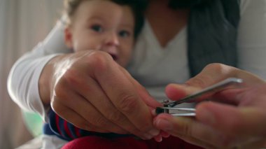 Anne tırnak makasıyla bebek tırnaklarını nazikçe kesiyor, ebeveyn yetiştirme anına yakın çekim yapıyor, bebek sakince izliyor, hijyen ve bakım yapıyor..