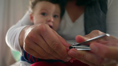 Anne tırnak makasıyla bebek tırnaklarını nazikçe kesiyor, ebeveyn yetiştirme anına yakın çekim yapıyor, bebek sakince izliyor, hijyen ve bakım yapıyor..