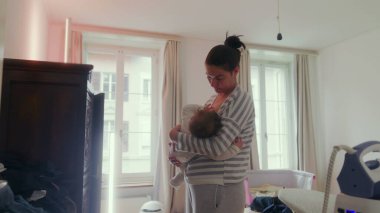Anne, bebeğini yatak odasında durup emzirirken huzur dolu bir yuva ortamında huzur verici, şefkatli bir an yaşıyor.