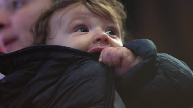 Bebek ceketi, yukarı bakıyor, kışlık palto giyiyor, sıcak aile manzarası, meraklı ve düşünceli ifade, sıcaklık ve koruma, günlük iç mekan sahnesi