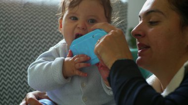 Bebek anne tarafından tutulurken mavi nesneyi çiğniyor, oyunculuk etkileşimine yakından bakıyor, bebek keşfi yapıyor, evde aile içi ilişkiler kuruyor, anne ile çocuk arasında hassas bir bağ kuruyor, bebek gülümsüyor..