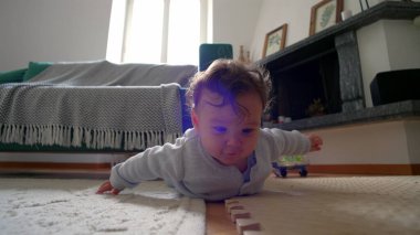 Bebek yerde yatıyor, iki koluyla itiyor, merakla ileri bakıyor, rahat bir yuva ortamında çevreyi keşfediyor, emeklemeyi öğrenmenin ilk aşamaları.