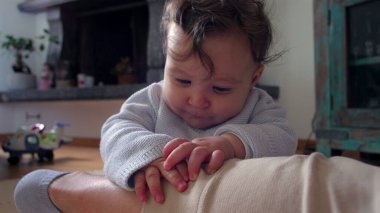 Bebek, anne bacağının üzerinde tuhaf bir ifadeyle dinleniyor, evde aile bağlarını kurma zamanı, bebek ve anne arasında oyuncu ve besleyici bir an, dokunsal bir merakla dünyayı keşfediyor..