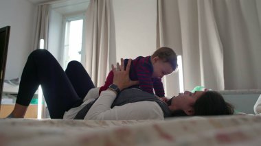 Anne yatakta uzanıyor, bebek üstte dinleniyor, neşeli ve samimi bir aile anı, sıcak bir ev ortamında bağ kuruyor ve rahatlıyor, birlikte vakit geçiriyoruz.