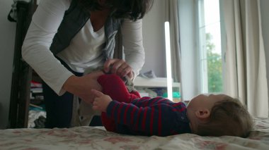 Anne bebek elbiselerini değiştirirken bebek yatakta yatar, hassas ve dikkatli bir şekilde bakım yapar, ev ortamında bebek hijyenine ve hijyene dikkat eder..