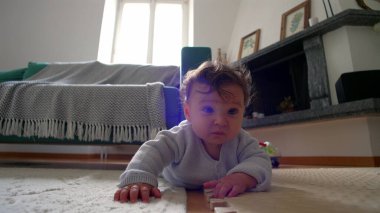 Bebek yerde yatıyor, iki koluyla itiyor, merakla ileri bakıyor, rahat bir yuva ortamında çevreyi keşfediyor, emeklemeyi öğrenmenin ilk aşamaları.