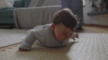 Bebek mindere uzanıyor, başını kaldırıyor ve odaklanmış ifade ile çevreyi keşfediyor, sakin bir ev ortamında erken gelişim ve motor becerilerle meşgul oluyor