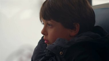 Hareket halindeki bir otobüsün penceresinde oturan genç çocuk, derin düşüncelere dalmış, sessizce geçen manzarayı seyrediyor.
