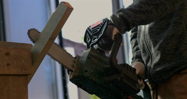 Testereyle odun kesen işçilerin yakın çekimi, 800 fps hızla uçan odun kıymıkları, hassasiyeti ve elektrikli testereyi kesmeye yoğun odaklanma.