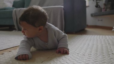 Bebek mindere uzanıyor, başını kaldırıyor ve odaklanmış ifade ile çevreyi keşfediyor, sakin bir ev ortamında erken gelişim ve motor becerilerle meşgul oluyor