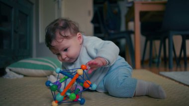 Bebek yerde yatıyor, ilginç bir şekilde renkli bir oyuncağı keşfediyor, güzel motor becerilerini geliştirirken çiğniyor, ev ortamında duyusal oyunlar oynuyor.