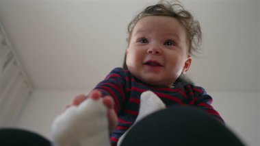 Anne bebeğin başını nazikçe tutuyor, bebek kucağında otururken neşeli bir etkileşim, aile evinde bir bağ kurma anı, ebeveynler ve çocuklar arasında bir bağ..