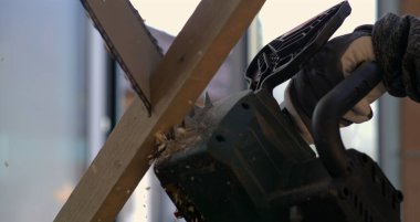 Tahtayı yavaş çekimde 800 fps hızla kesen elektrikli testerenin yakın çekimi. Tahta kıymıkları uçuşuyor. Kesme hareketine ve elektrikli testere hassasiyetine odaklanıyor.