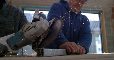 Açı öğütücüyle metal kesen işçiler, başka bir işçi metali sabit tutarken kıvılcımlar uçuşuyor, takım çalışması ve hassasiyeti vurgulanıyor, 800 fps yavaş çekim