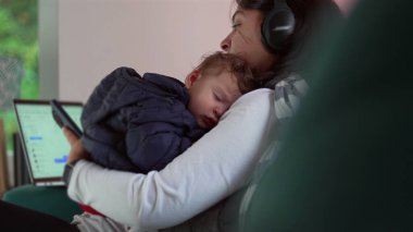 Anne telefonunu kullanırken uyumakta olan bebeği kucağında tutuyor ve dizüstü bilgisayarını kontrol ediyor, iş ve bakıcılık arasında birden fazla iş yapıyor, aile ve kariyer sorumluluklarını birbirine karıştırıyor.