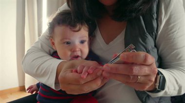 Anne, bebek tırnaklarını kesiyor, bakımını yapıyor ve bakım görüyor. Bebek hijyenine odaklanıyor. Bebek bakımını yakından izliyor..