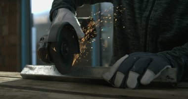 Açı öğütücüsünün metali kesmesi, kıvılcımların uçuşması, eldivenli zanaatkarlara odaklanmak, hassas metal işçiliği, yoğun konsantrasyon.