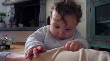 Bebek, anne bacağının üzerinde tuhaf bir ifadeyle dinleniyor, evde aile bağlarını kurma zamanı, bebek ve anne arasında oyuncu ve besleyici bir an, dokunsal bir merakla dünyayı keşfediyor..