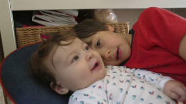 Bebek bir fedaiye uzanıyor, ağabeyinin yüzüne dokunuyor, evde sakin bir aile ortamında nazik bir kardeş etkileşimi.