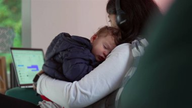 Anne telefonunu kullanırken uyumakta olan bebeği kucağında tutuyor ve dizüstü bilgisayarını kontrol ediyor, iş ve bakıcılık arasında birden fazla iş yapıyor, aile ve kariyer sorumluluklarını birbirine karıştırıyor.