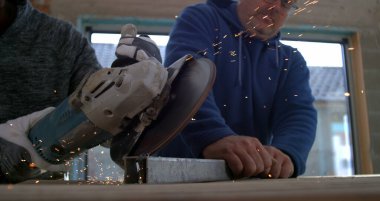 Açı öğütücüyle metal kesen işçiler, başka bir işçi metali sabit tutarken kıvılcımlar uçuşuyor, takım çalışması ve hassasiyeti vurgulanıyor, 800 fps yavaş çekim
