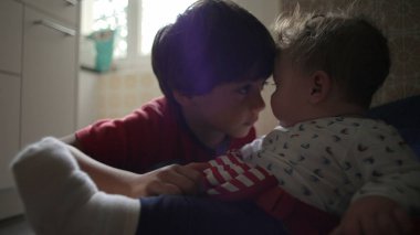 Bebek bir fedainin ayaklarını tekmeliyor. Bu arada abim de günlük aile rutini sırasında mutfakta sakin ve sevgi dolu bir kardeş sohbeti izliyor.