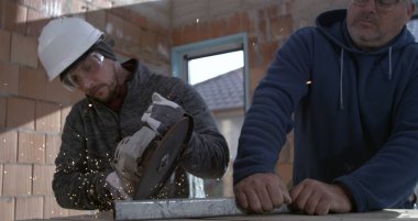 Açı öğütücü metal kesimi sırasında kıvılcımlar çakıyor, koruyucu ekipmanlı işçiler inşaat işinde işbirliği yapıyor, sanayi bölgesi süper yavaş çekim altında.