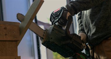 Testereyle odun kesen işçilerin yakın çekimi, 800 fps hızla uçan odun kıymıkları, hassasiyeti ve elektrikli testereyi kesmeye yoğun odaklanma.